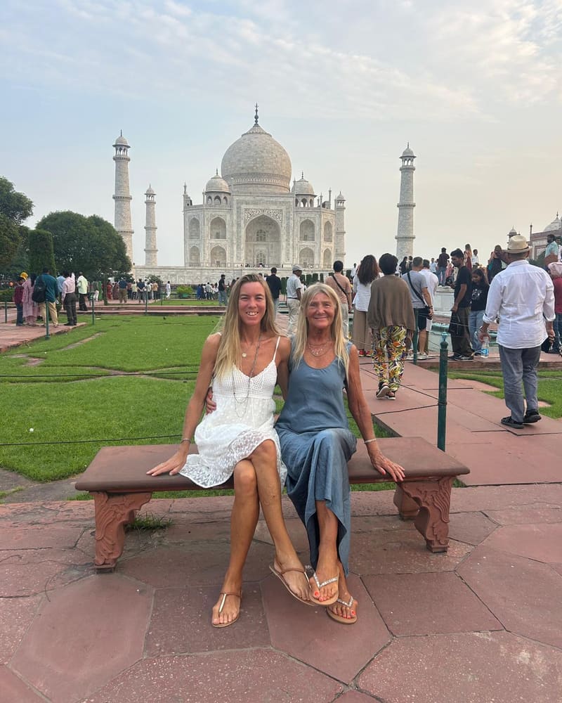 Two travellers smiling on a red sandstone bench in the gardens of the Taj Mahal